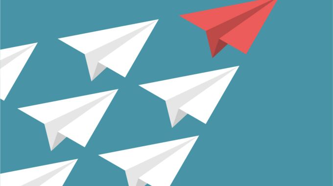 weiße Papierflieger folgen rotem Papierflieger als Symbolbild für das Thema „Führungskompetenz - Stärken stärken”