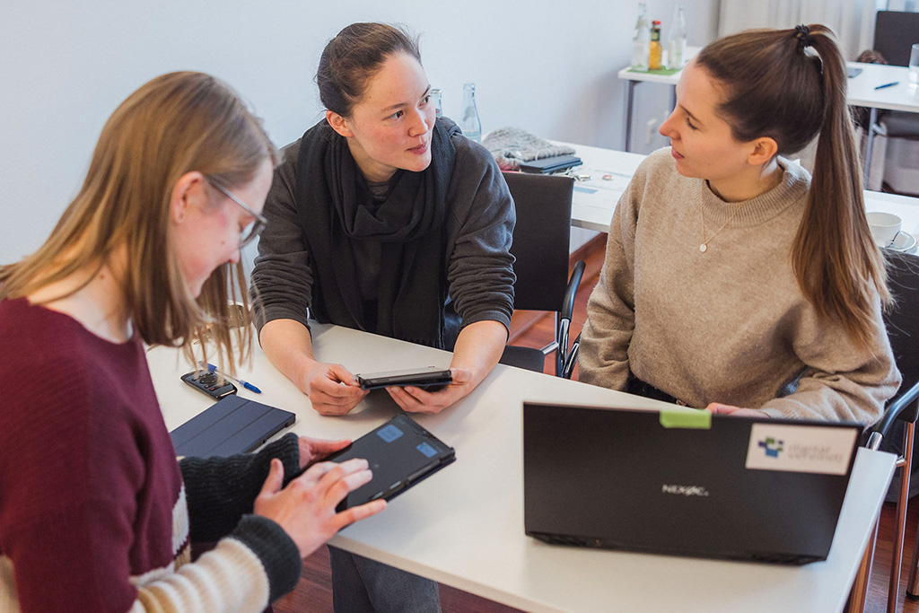 Drei Mitarbeiterinnen nutzen im Workshop digitale Medien, um sich über ihre Prozesse der täglichen Arbeit auszutauschen